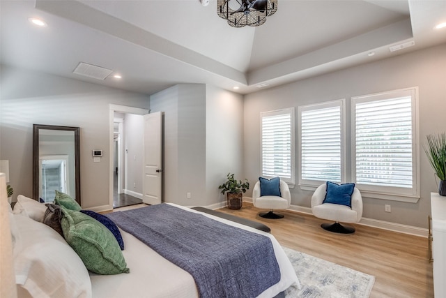 bedroom with multiple windows, a raised ceiling, a chandelier, and light hardwood / wood-style floors