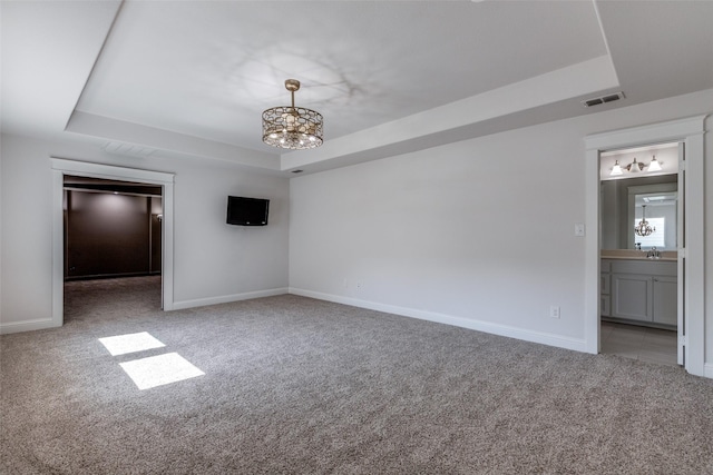 unfurnished bedroom with sink, ensuite bath, carpet floors, a raised ceiling, and a chandelier