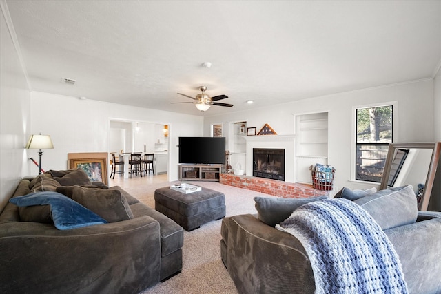 living room featuring built in shelves, a fireplace, light colored carpet, and ceiling fan