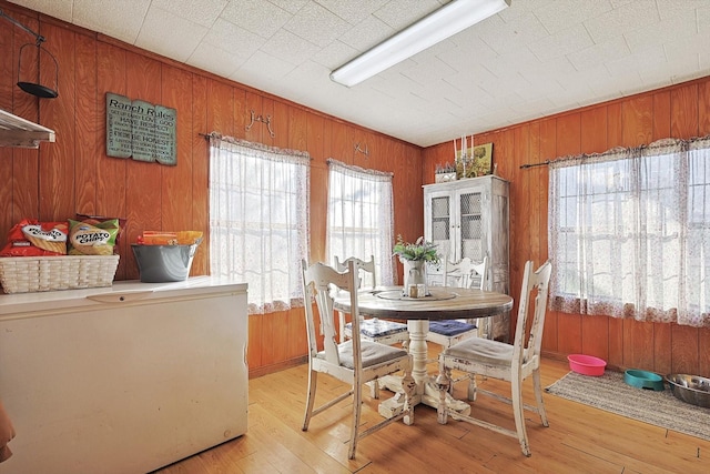 dining space with light hardwood / wood-style floors and wood walls