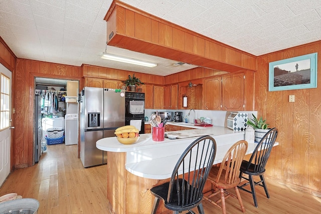 kitchen with stainless steel fridge, washer / dryer, kitchen peninsula, and light hardwood / wood-style flooring