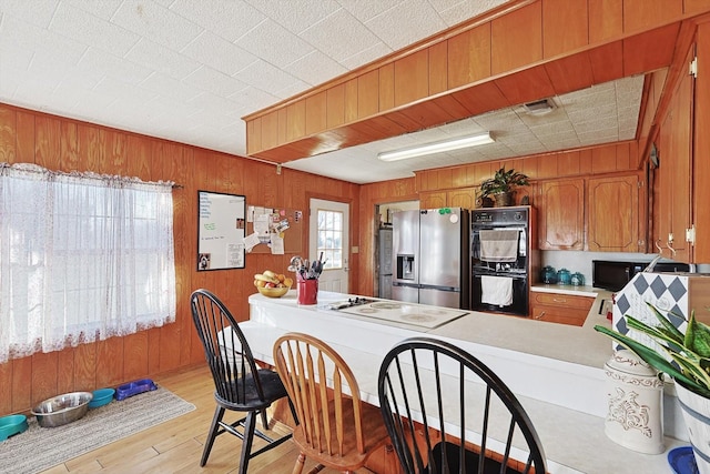 kitchen with stainless steel fridge, double oven, light hardwood / wood-style floors, white electric stovetop, and wood walls