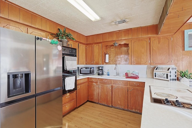 kitchen featuring wooden walls, sink, appliances with stainless steel finishes, and light hardwood / wood-style flooring