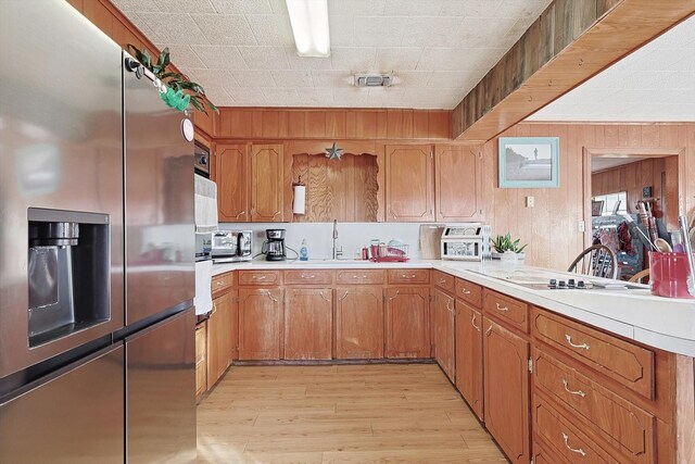 kitchen with wood walls, oven, sink, stainless steel refrigerator with ice dispenser, and light hardwood / wood-style flooring