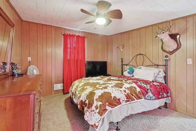 bedroom with ceiling fan, carpet, and wood walls