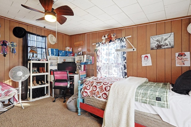 carpeted bedroom featuring ceiling fan and wooden walls