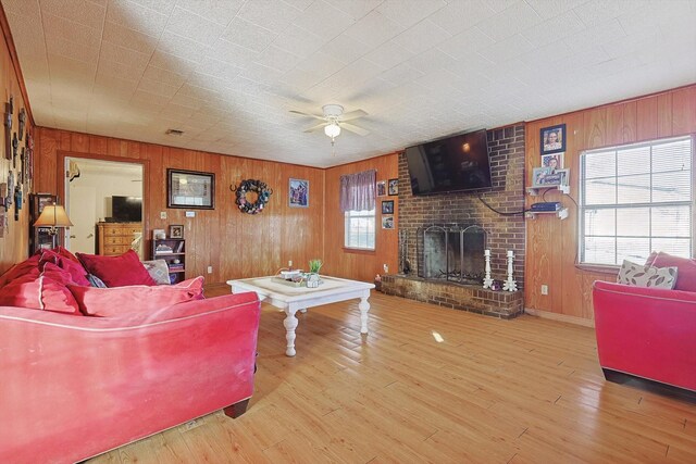 living room with ceiling fan, light hardwood / wood-style flooring, wooden walls, and a brick fireplace