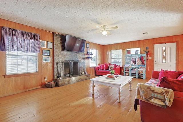 living room with hardwood / wood-style flooring, ceiling fan, wood walls, and a brick fireplace