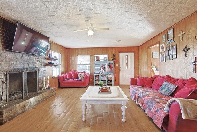 living room featuring ceiling fan, light hardwood / wood-style floors, wood walls, and a brick fireplace