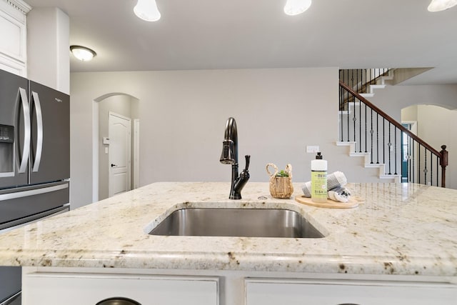 kitchen with a sink, arched walkways, white cabinets, and stainless steel fridge with ice dispenser