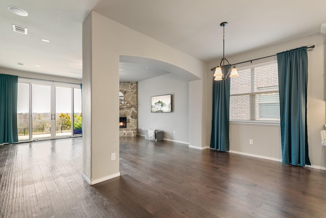 unfurnished room with visible vents, baseboards, a stone fireplace, and wood finished floors