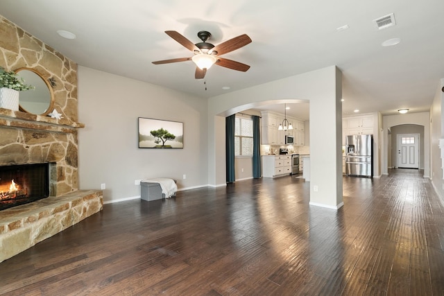 unfurnished living room featuring visible vents, dark wood-type flooring, baseboards, a fireplace, and arched walkways