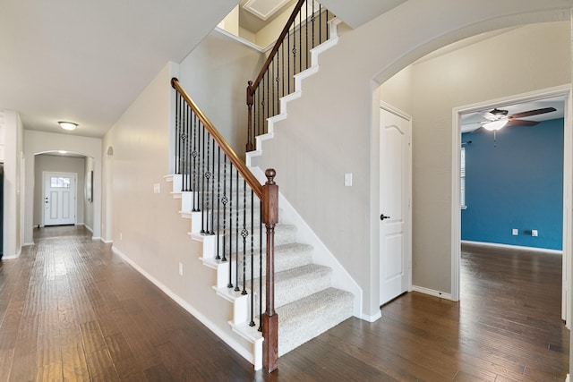 staircase with arched walkways, ceiling fan, baseboards, and wood finished floors