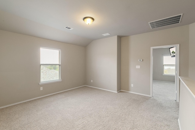 empty room featuring visible vents, baseboards, light colored carpet, and vaulted ceiling