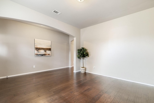 spare room featuring arched walkways, visible vents, baseboards, and wood finished floors