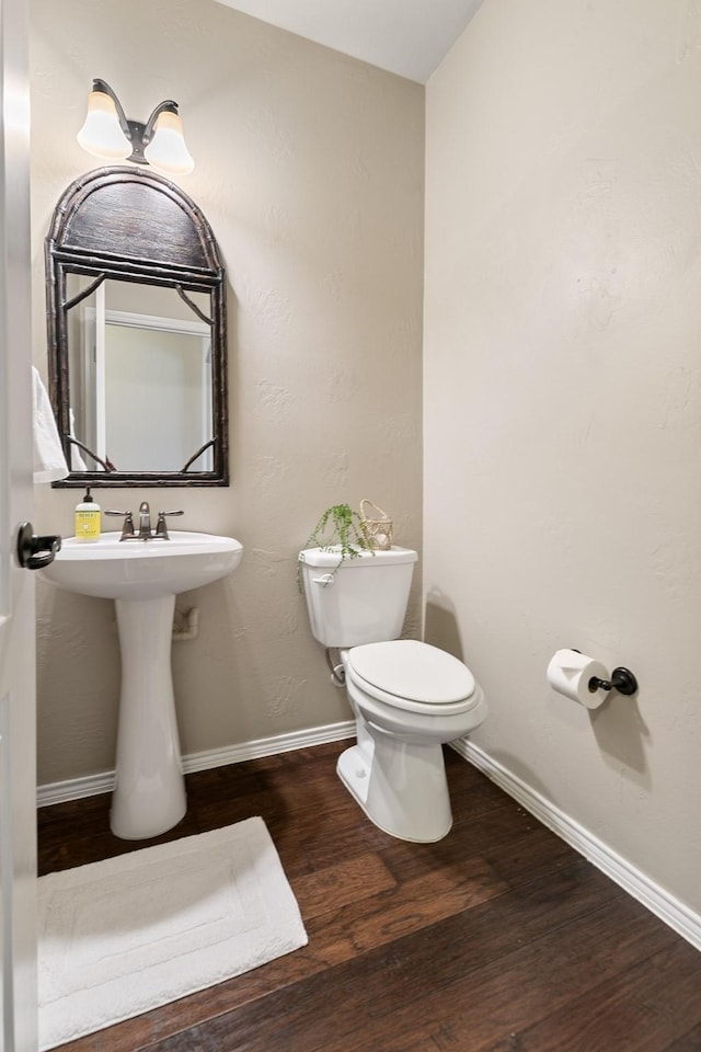 half bathroom featuring toilet, wood finished floors, and baseboards