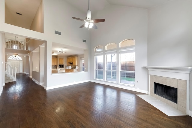 unfurnished living room featuring a high ceiling, dark hardwood / wood-style flooring, ceiling fan, and a tiled fireplace