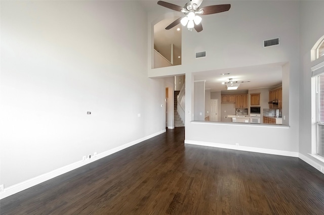 unfurnished living room with ceiling fan, dark hardwood / wood-style floors, and a high ceiling