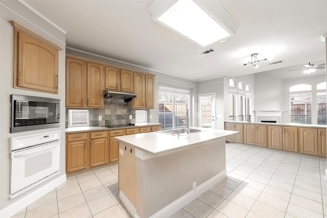 kitchen featuring built in microwave, tasteful backsplash, oven, black electric cooktop, and a center island with sink