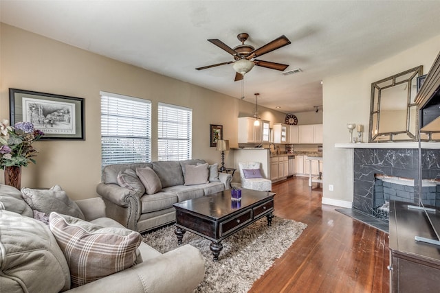 living room featuring dark hardwood / wood-style flooring, a premium fireplace, ceiling fan, and sink