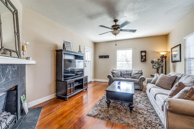 living room featuring a high end fireplace, wood-type flooring, a textured ceiling, and ceiling fan