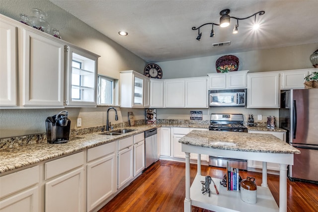 kitchen with dark wood-type flooring, white cabinets, sink, appliances with stainless steel finishes, and light stone counters