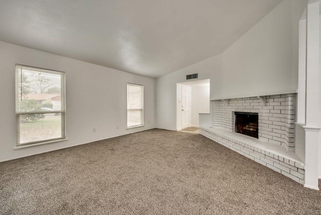 unfurnished living room featuring lofted ceiling, carpet floors, a brick fireplace, and a wealth of natural light