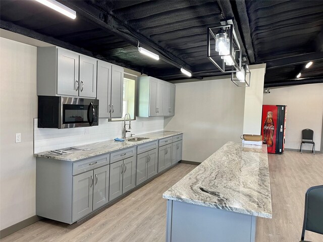 kitchen featuring gray cabinetry, sink, tasteful backsplash, light hardwood / wood-style floors, and light stone counters