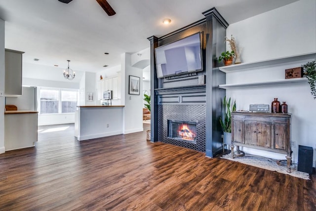 unfurnished living room featuring ceiling fan with notable chandelier, wood finished floors, a tile fireplace, and baseboards