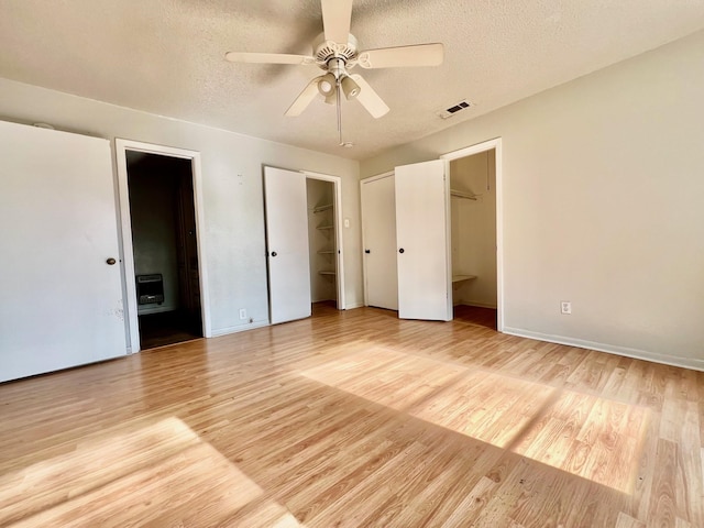 unfurnished bedroom featuring ensuite bath, heating unit, a textured ceiling, and light hardwood / wood-style flooring