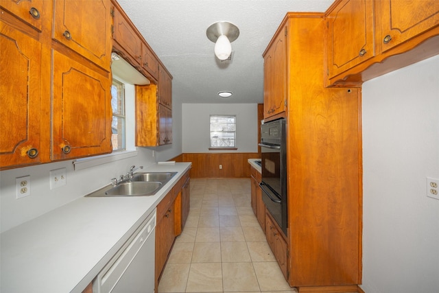 kitchen with white dishwasher, sink, wooden walls, a textured ceiling, and black oven