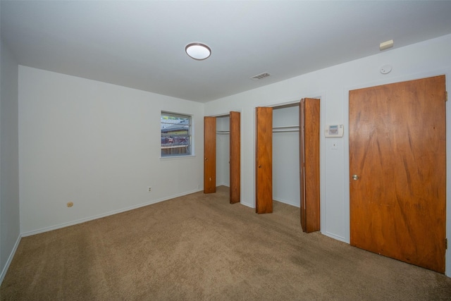 unfurnished bedroom featuring light colored carpet and multiple closets