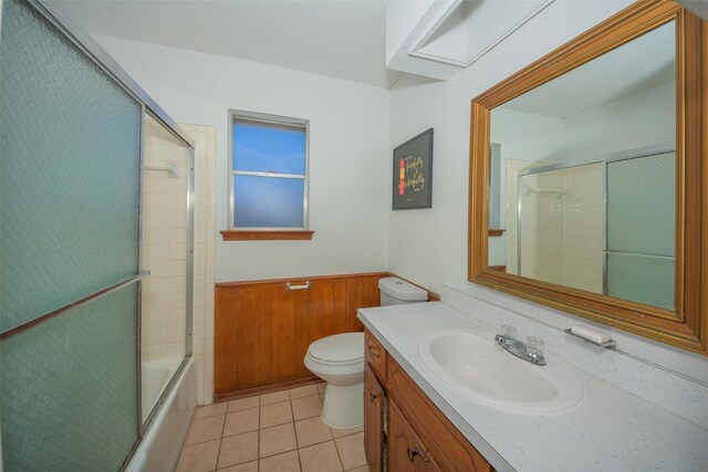 full bathroom featuring tile patterned floors, combined bath / shower with glass door, wooden walls, toilet, and vanity