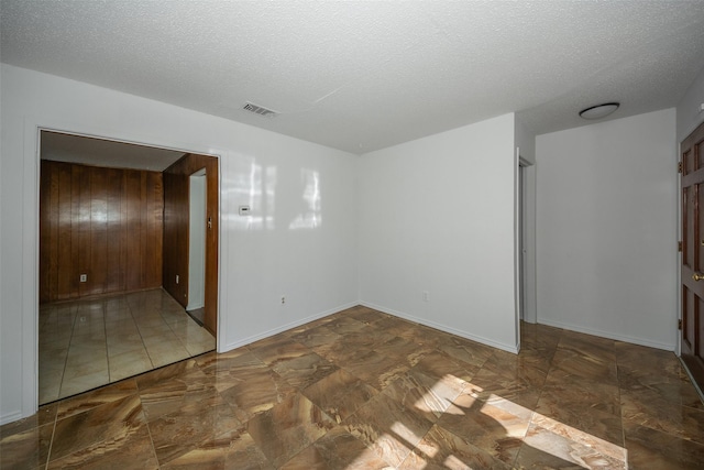 empty room featuring a textured ceiling and wooden walls