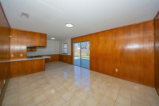 kitchen featuring kitchen peninsula, gas cooktop, a textured ceiling, light tile patterned floors, and wood walls