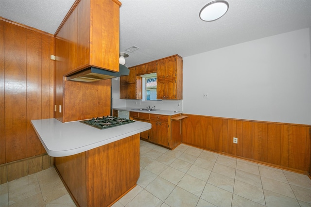 kitchen featuring stainless steel gas stovetop, wood walls, ventilation hood, a textured ceiling, and kitchen peninsula