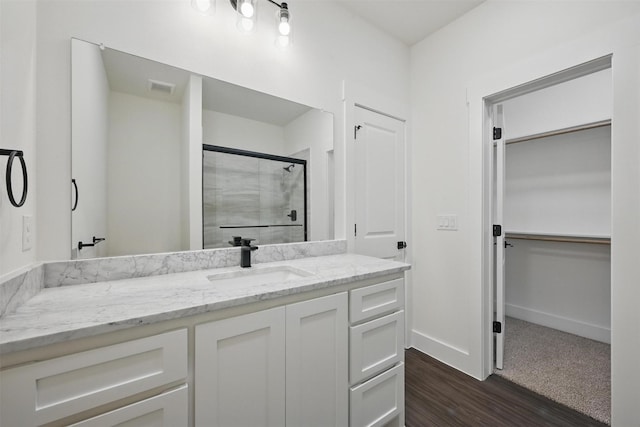 full bath with vanity, baseboards, a stall shower, visible vents, and wood finished floors