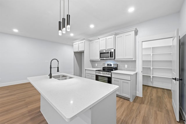 kitchen with appliances with stainless steel finishes, sink, white cabinetry, hanging light fixtures, and an island with sink