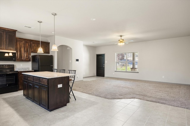 kitchen with dark brown cabinetry, ceiling fan, a center island, light colored carpet, and black appliances