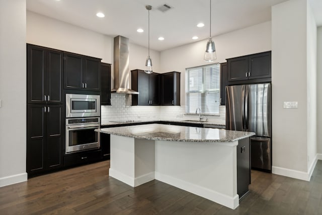 kitchen featuring light stone countertops, a center island, wall chimney exhaust hood, pendant lighting, and appliances with stainless steel finishes