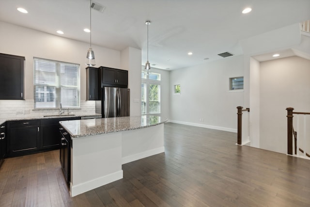 kitchen with stainless steel fridge, light stone counters, sink, decorative light fixtures, and a kitchen island