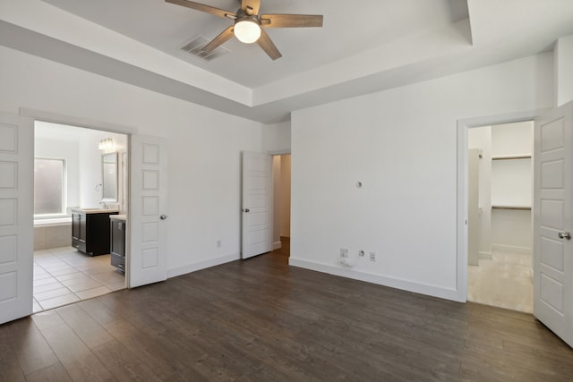 unfurnished bedroom with connected bathroom, a tray ceiling, ceiling fan, and dark wood-type flooring