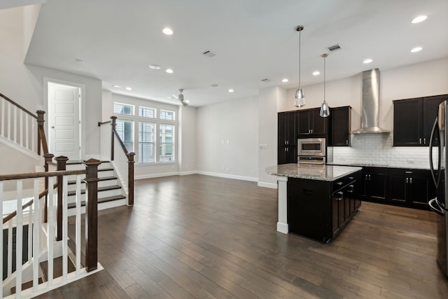 kitchen featuring pendant lighting, a center island, wall chimney exhaust hood, ceiling fan, and appliances with stainless steel finishes