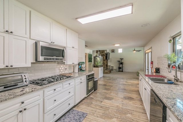 kitchen featuring black appliances, sink, ceiling fan, light stone countertops, and white cabinetry