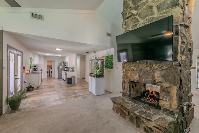 living room featuring french doors, a stone fireplace, light hardwood / wood-style flooring, and lofted ceiling