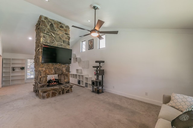 carpeted living room with a stone fireplace, ceiling fan, built in shelves, and lofted ceiling