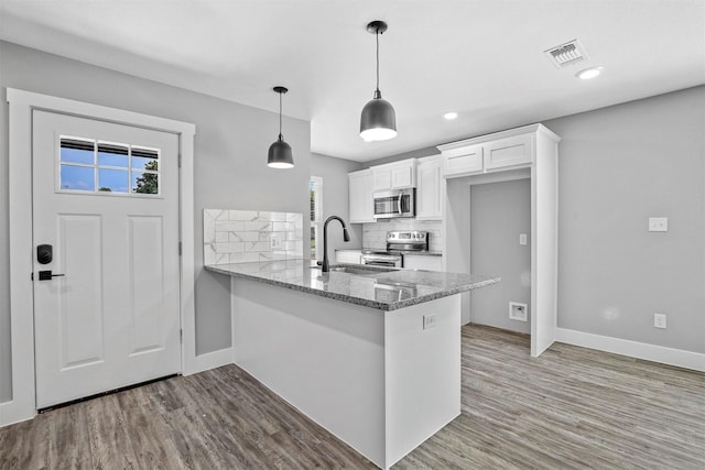 kitchen with kitchen peninsula, appliances with stainless steel finishes, sink, stone countertops, and white cabinets