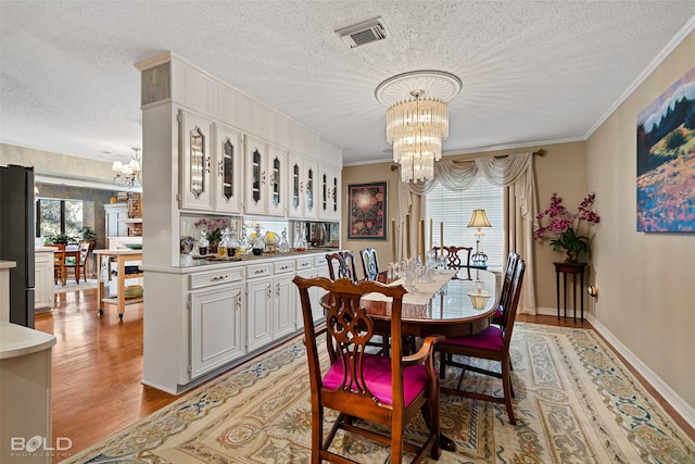 dining area with light hardwood / wood-style floors, a chandelier, crown molding, and a textured ceiling