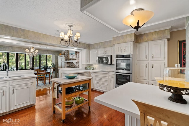 kitchen featuring sink, white cabinetry, stainless steel appliances, a notable chandelier, and decorative light fixtures