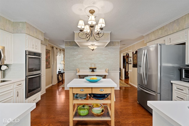 kitchen with a chandelier, ornamental molding, appliances with stainless steel finishes, pendant lighting, and white cabinets